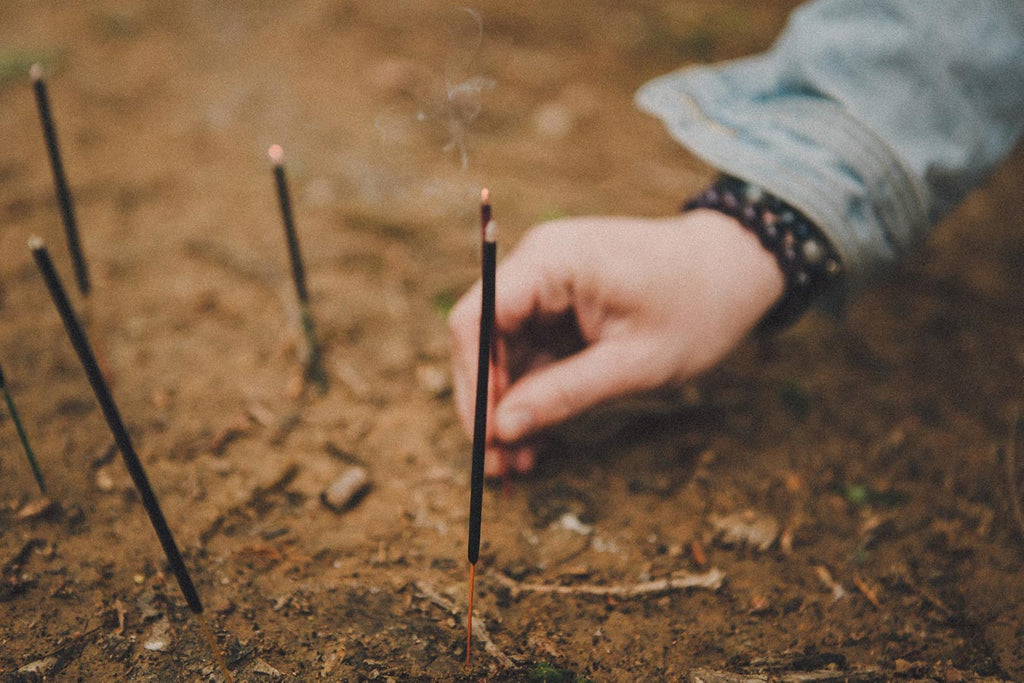 Hand reaching for incense sticks in the dirt
