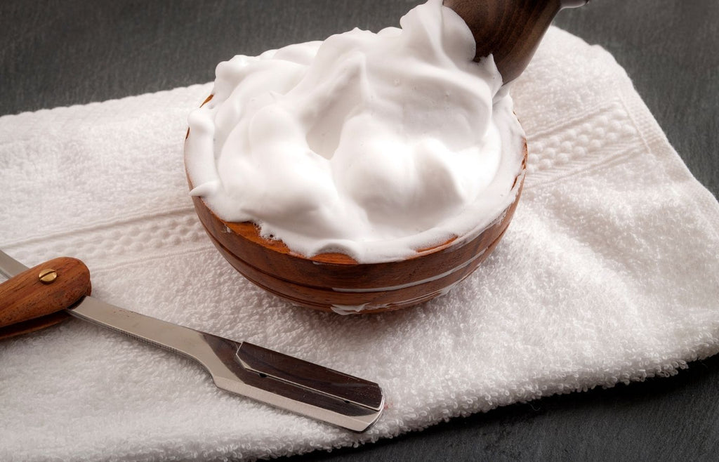 Homemade shaving cream in a bowl on a towel with a razor next to it.