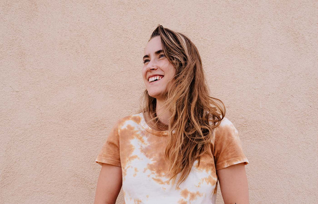 Woman in tie dye smiling in front of a plain wall