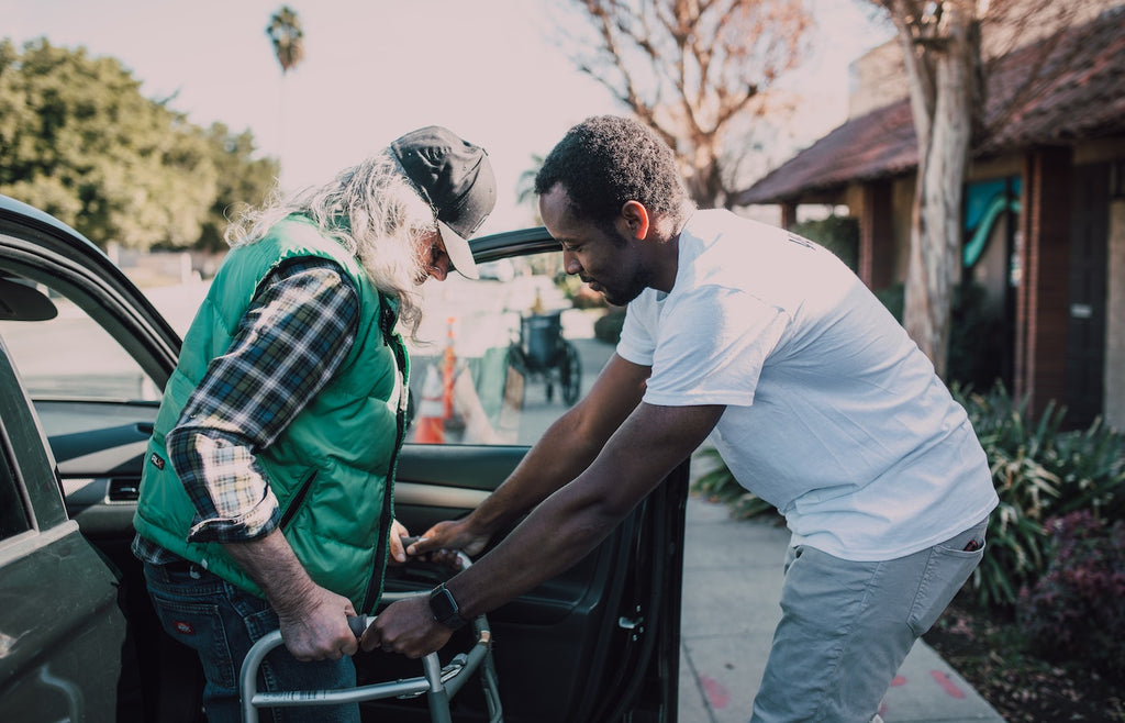 Younger man helping older man exit car with his walker