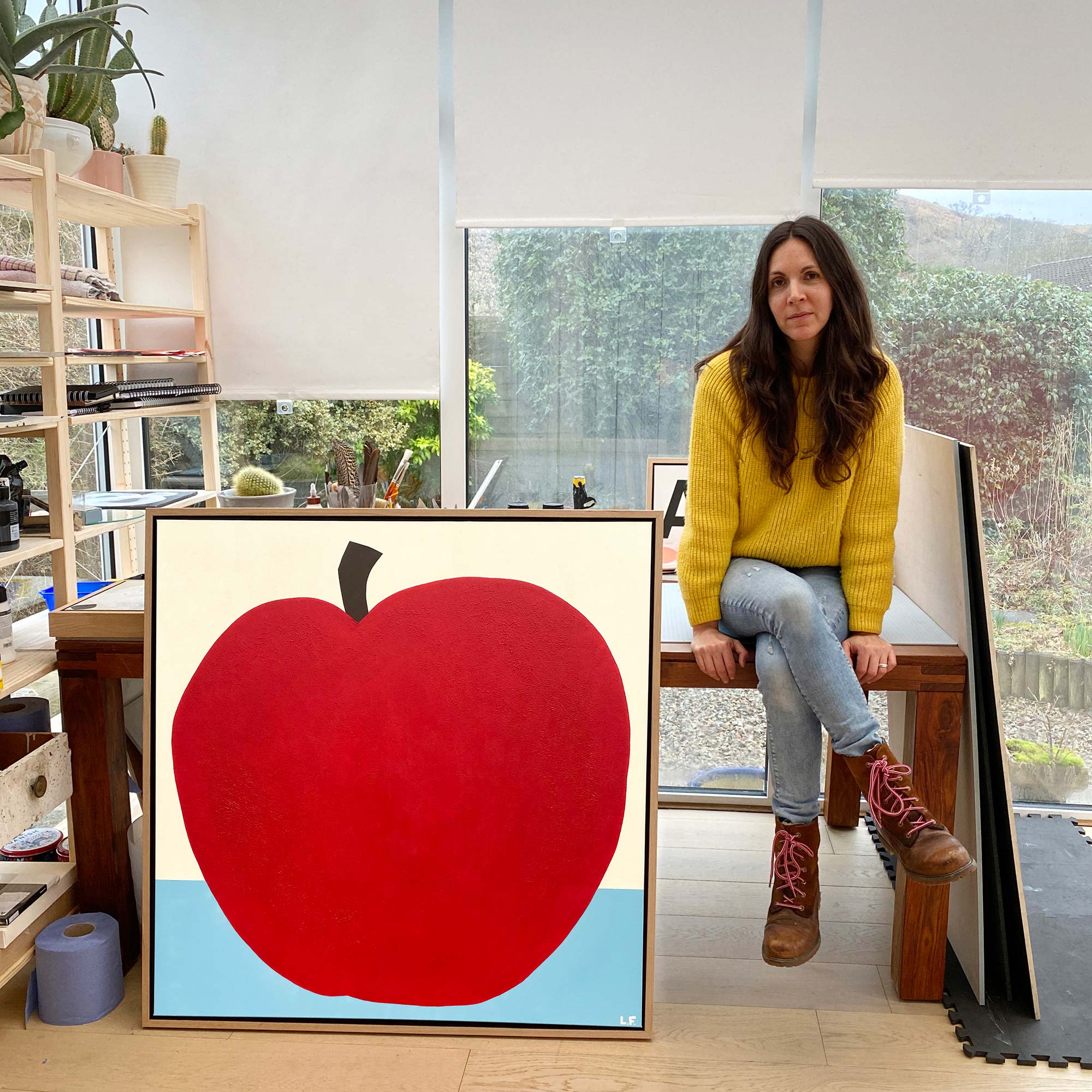 Lorna sitting on a table next to a painting of a huge apple