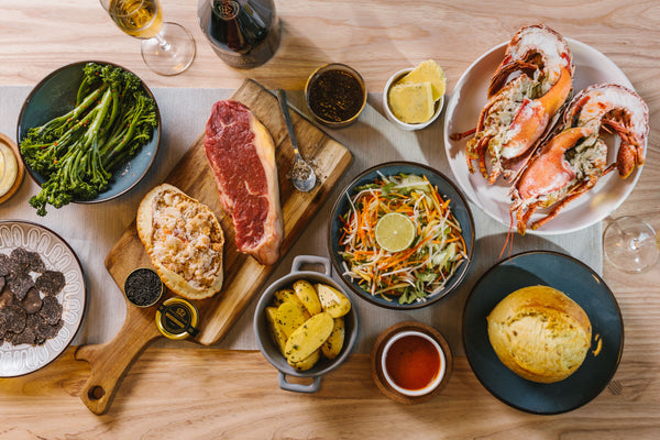 a table of fine-dining food including lobster, steak, crab and a variety of sides