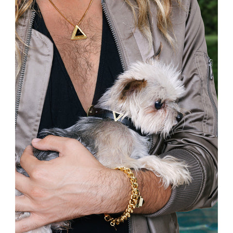 Man with open deep v neck shirt wearing a gorgeous DIPHDA Gold Stellar Onyx Necklace. It's Triangle shape is unique and he's holding his cute fluffy little dog who's wearing the matching Jet Black Onyx Collar Charm Set. His wrist is sporting an Iconic Triangle Onyx Bracelet with a thick gold curb chain and awesome big unique clasp.