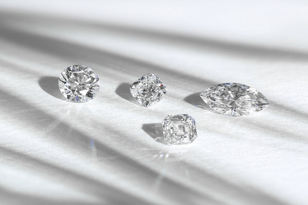 Marquise diamond, round brilliant cut diamond, cushion cut diamond and asscher cut diamond scattered on a grey table