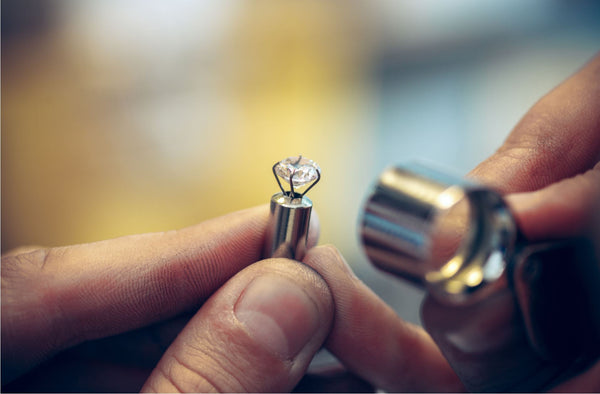 close up of jeweller hands holding a loupe inspecting a diamond from the side