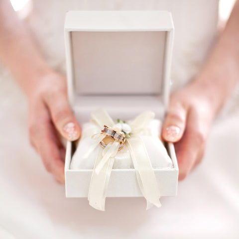 Close up of bride holding a jewellery box with a bow tying two wedding bands together