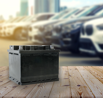 Car battery on wooden table on blurred car park row on background.