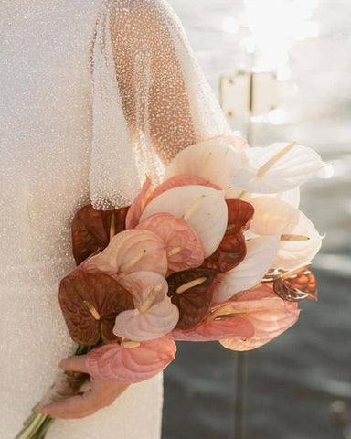 Image of woman holding anthurium bouquet. Blooms are white, pink, and dark red.