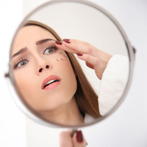 A woman looking in a mirror and noticing her lashes are shedding