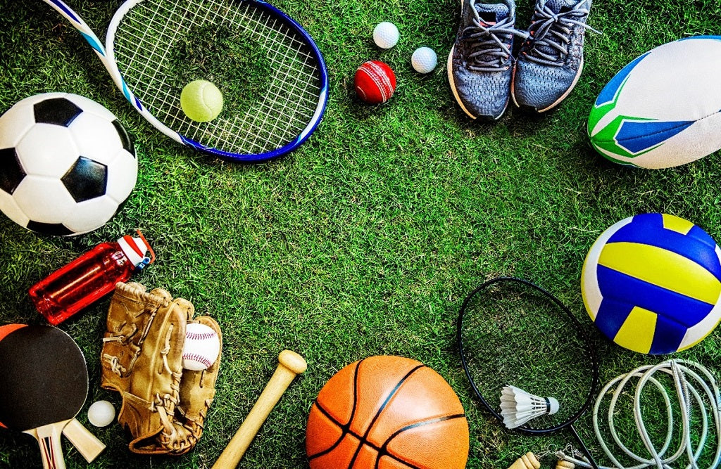 芝生にテニスラケット、バスケットボール、バレーボール、サッカーボール、ラグビーボール、卓球ラケット、 バドミントンラケット、野球グローブ、スパイクが置いてあります