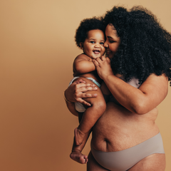Person of colour care giver holding a baby and smiling. The birth giver's body has stretch marks