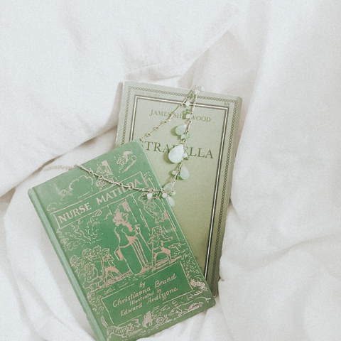 Green hued books nestle gently amongst soft linens adorned by a green necklace