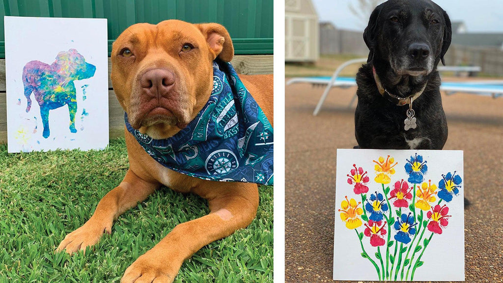 Two dogs posing with artwork made with their paw prints