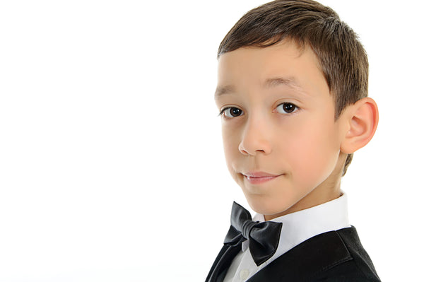 Photo of a young boy wearing a dapper bow tie, an essential accessory to complete a boys' tuxedo ensemble, ideal for formal occasions