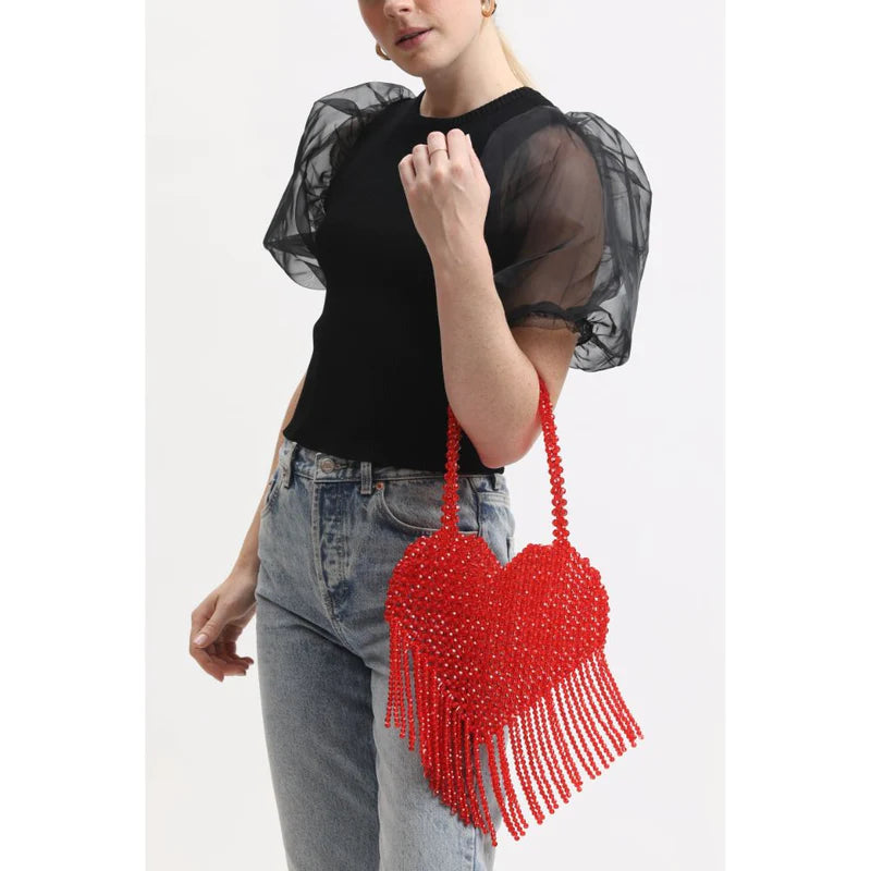 Woman holding a sparkly red heart-shaped bag with fringe