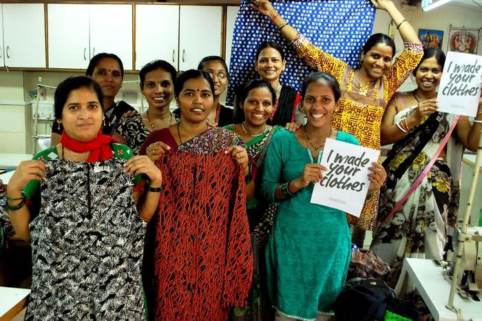 Mujeres de Creative Handicrafts sosteniendo el cartel "I made your clothes" (Yo hice tu ropa)
