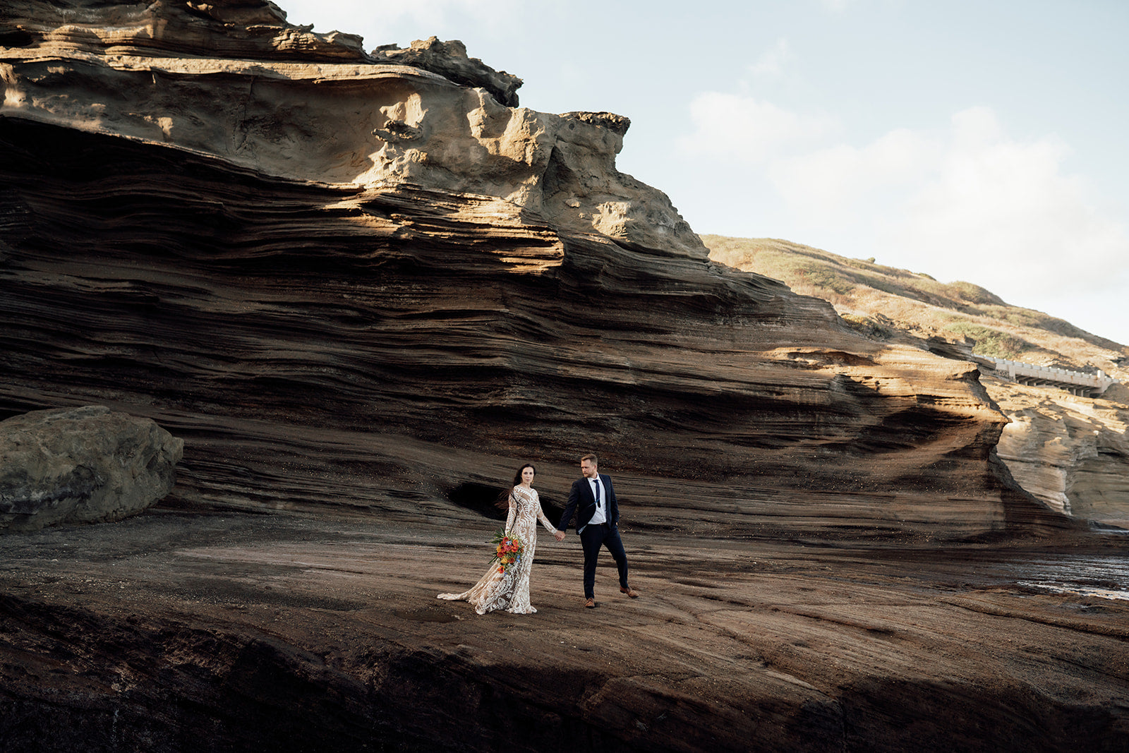 A couple with a bouquet walking along the rocks in Hawaii