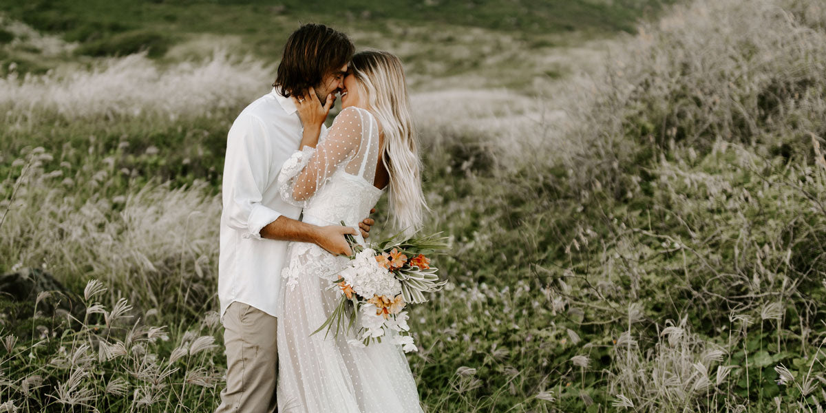 A couple just married holding a bouquet and embracing in a field