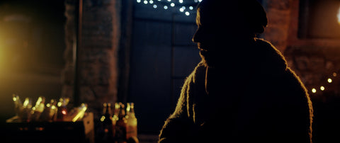 Photo of Joe sat almost in silhouette with fairy lights behind him and cider bottles in the background.