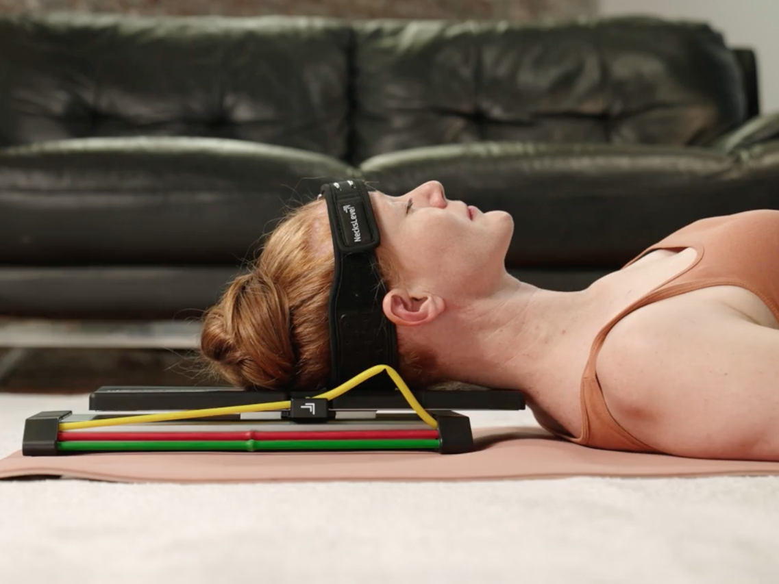 Woman lying on a yoga mat with a neck massager, eyes closed, relaxed posture.