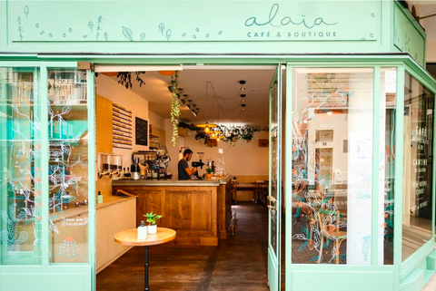 Porte d'entrée verte de coffee shop Alaïa avec une petite table juste derrière la porte