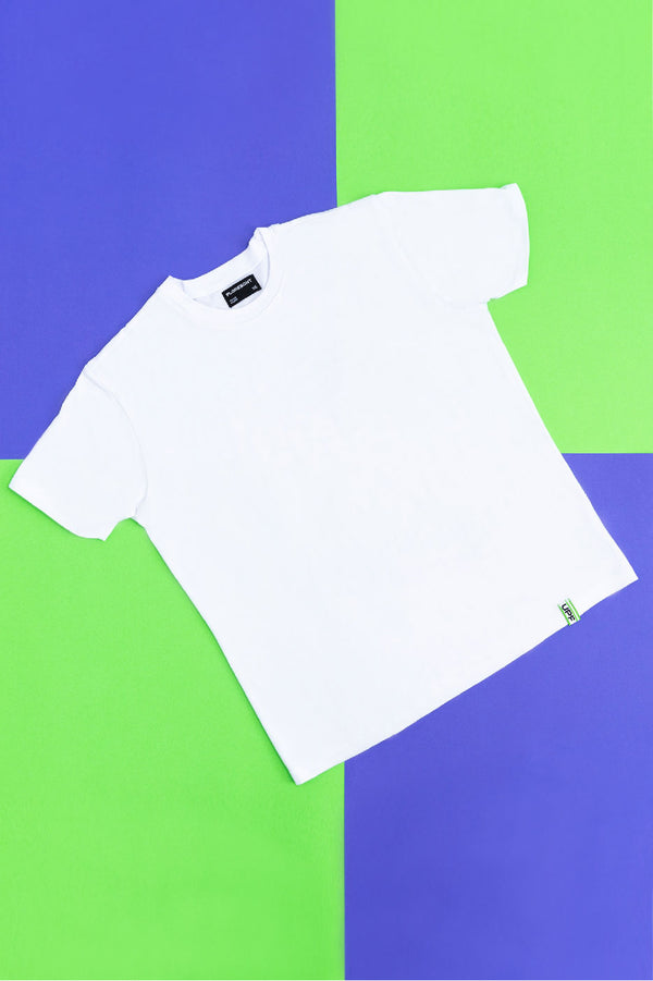 Flat lay of white UV resistant t-shirt with green UPF 50+ logo tab at hem on top of green and blue checkered background by Florescnt.