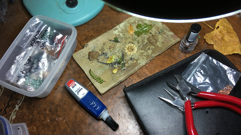 Seeds and leaves that have been sealed with acrylic, with red handled pliers to rights and superglue to lefy