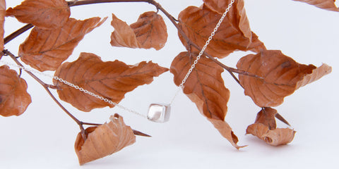 Sterling silver cube necklace dangling from russet leaved branch