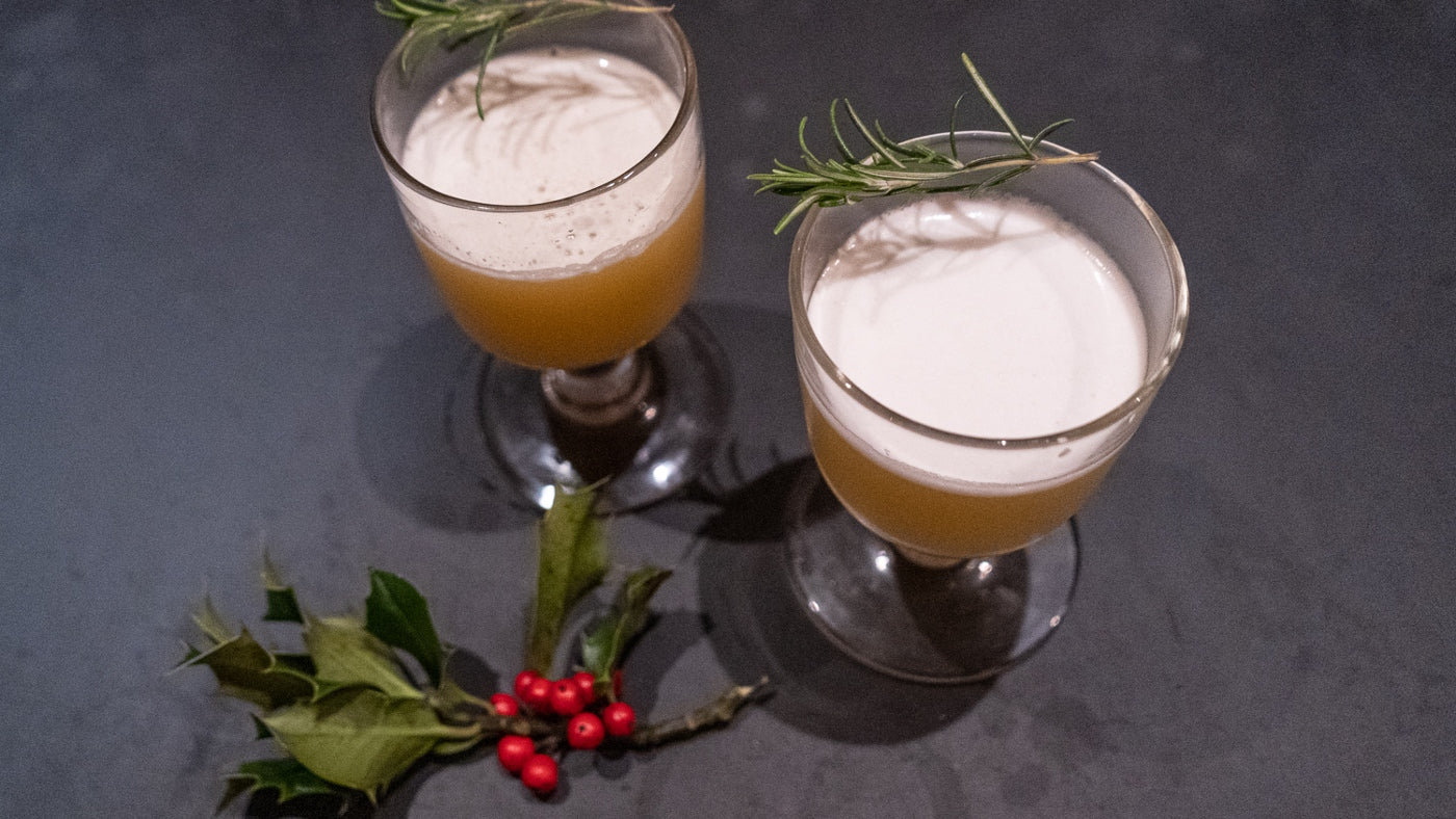 Two matching glasses of Sour Cocktail, rosemary garnish and decorative holly spring