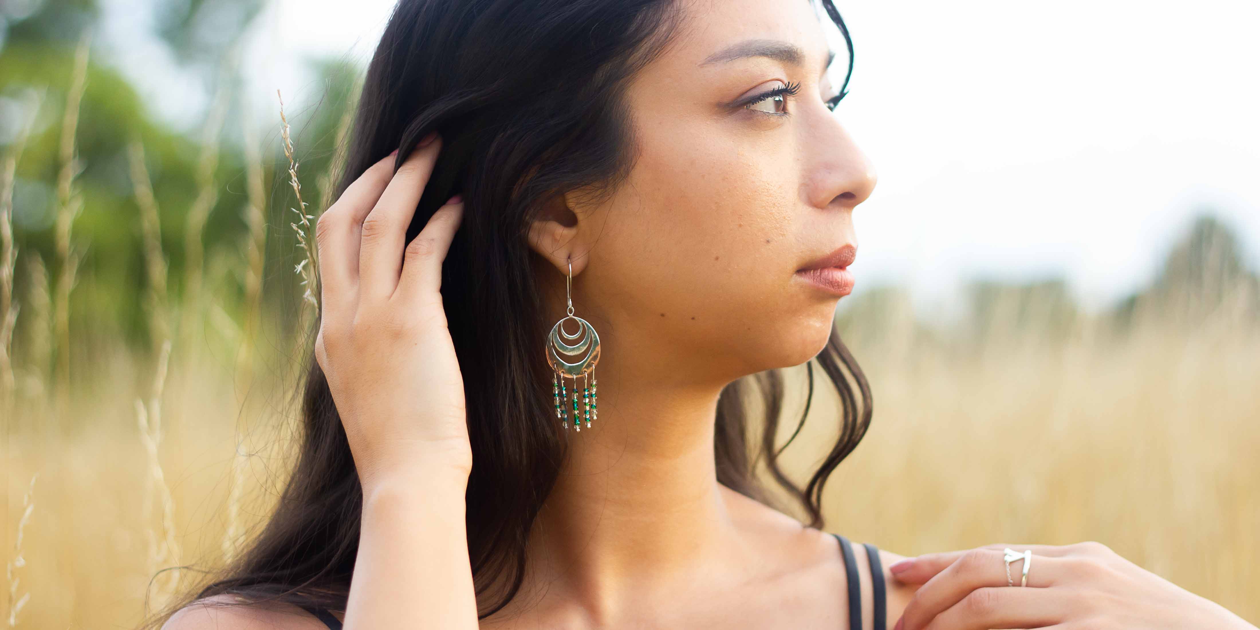 Woman wearing silver and copper earrings with beads, looks across field of golden grass