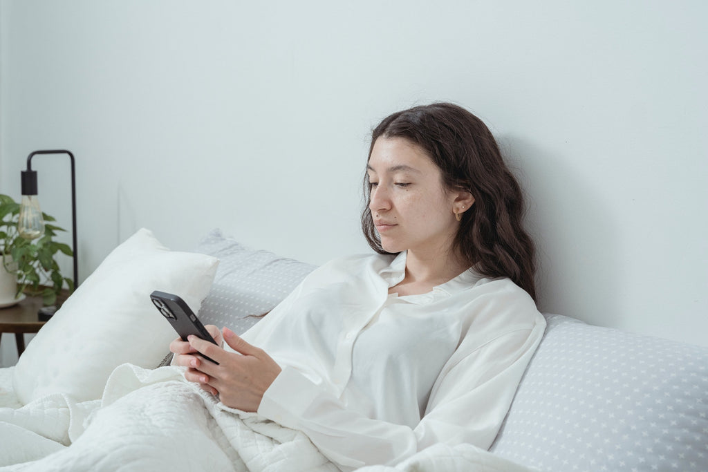 Vrouw op telefoon in bed - tips voor betere nachtrust met aroma diffuser en essentiële oliën van Happy Cloud