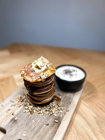 Stablede blåbær pandekager med smørklatten og granola, serveret med yoghurt og chiafrø, præsenteret på et træskærebræt - Danish Granola Company.