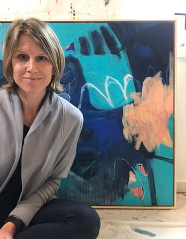 White woman sitting on the floor in front of a abstract painting