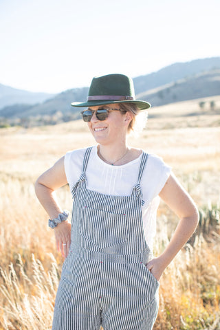 White woman in overalls outside in a field in front of mountains