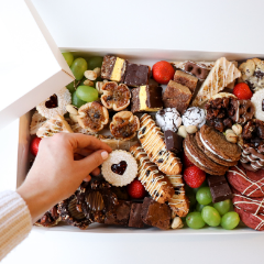 Trove Desserts Large Christmas Dessert Box with an assorted selection of seasonal holiday treats with a hand picking up a heart shaped linzer cookie out of the box