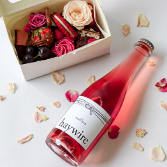 Trove Desserts Sweetheart Bundle including a mini grazing style dessert box for Valentine's day in pink and red theme and a 375mL bottle of Okanagan Crushpad's Haywire Baby Bub Sparkling Rose pictured with scattered rose petals