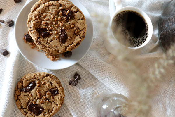 A stack of chocolate chip cookies on a plate with dark chocolate chunks and a black cup of coffee.