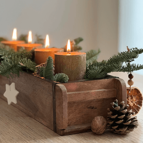Holzkiste mit Weihnachtsdeko, flackernde Kerzen, Tannenzweige, Zapfen, Orange Scheiben