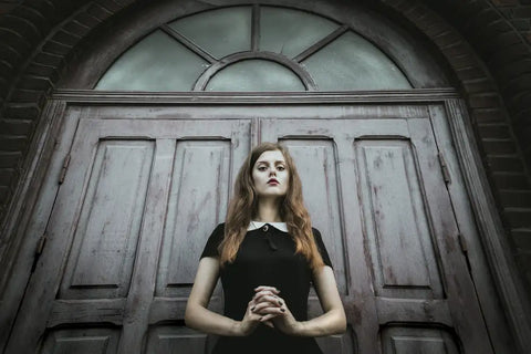 goth girl with clasped hands standing in front of double doors