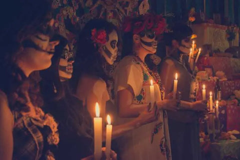 mexican people holding candles with faces painted like skulls