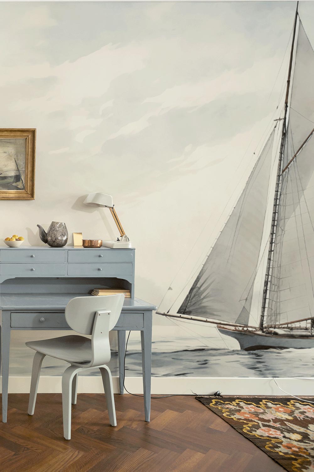 Sail boat and ocean scene shown on wall behind vintage blue desk in a front entry way.