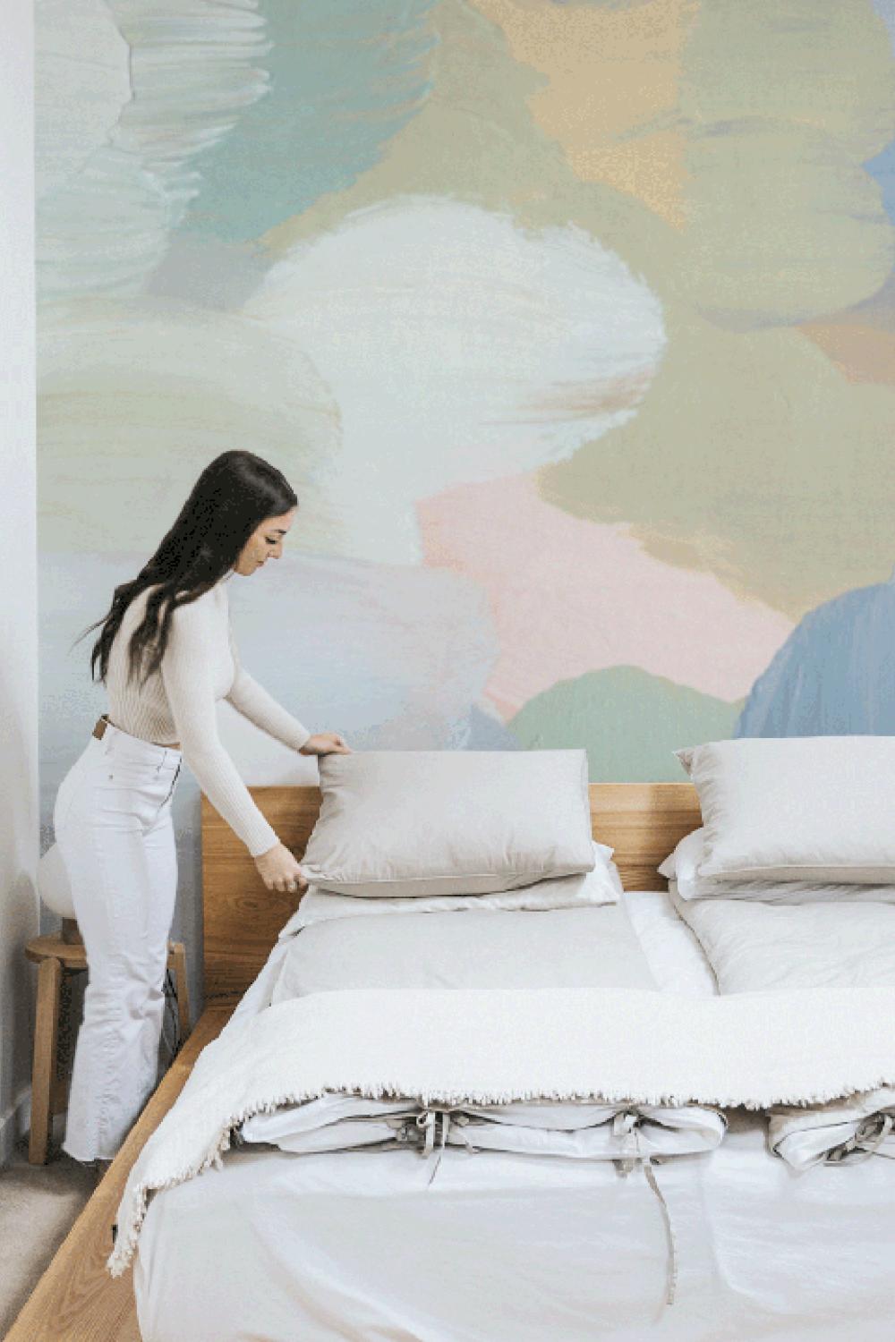 girl making bed in front of abstract wall mural