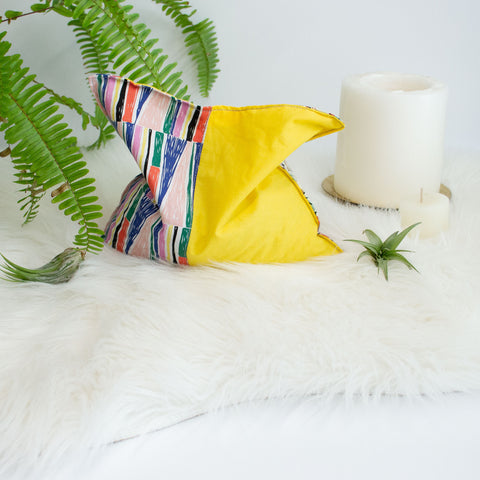 colorful cherry pit grain bag is surrounded by candles, air plants, and a fern on a faux fur blanket.