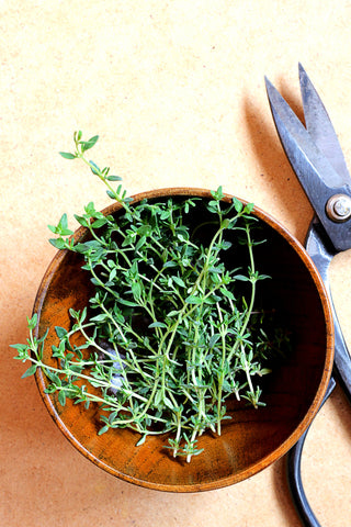 A bunch of fresh thyme in a wooden bowl. A pair of kitchen shears sit next to the bowl on a light wooden counter