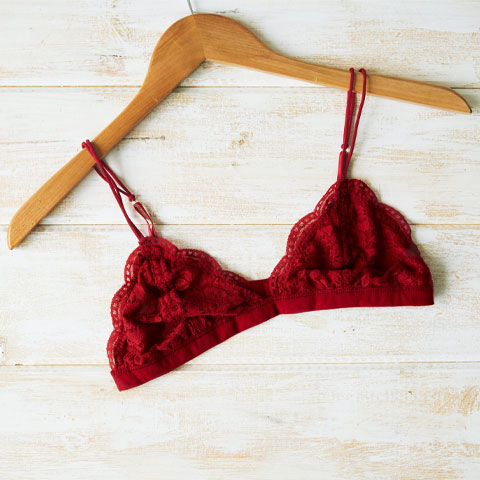 red lacy triangle bra hangs on wood hanger on a light wood background