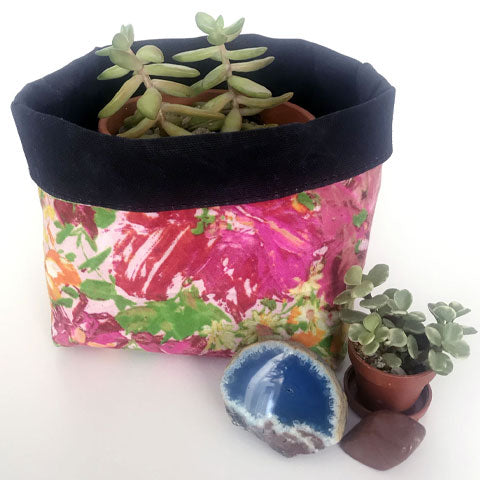Pink and black waxed canvas organizer holds a succulent plant. A miniature succulent plant and blue geode sits next to the holder. 