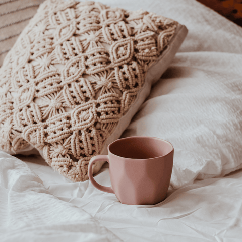 small mug on a bed next to a soft pillow