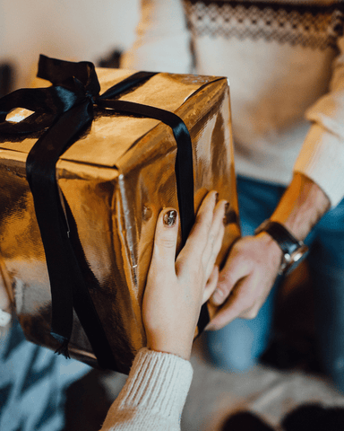 one person handling a beautiful brown gift box with a black ribbon to another person