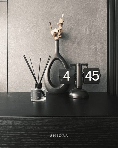 beautiful black clock next to a piece of art flower vase and shiora's reed diffusers