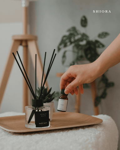 A person picking up shiora's essential oils next to shiora's reed diffuser on a wooden tray